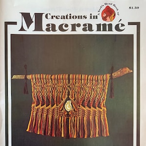 Op de afbeelding: Een boek getiteld "A Turk's Head Book of Creations in Macrame" met een prijs van $ 1,50. De omslag toont een kleurrijk macramé wandkleed met een schelp in het midden.