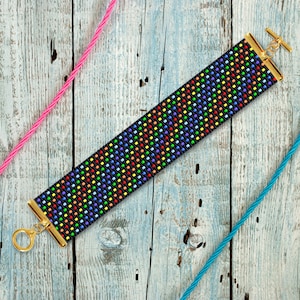 May include: A black beaded bracelet with a rainbow pattern and gold clasps. The bracelet is lying on a wooden surface.