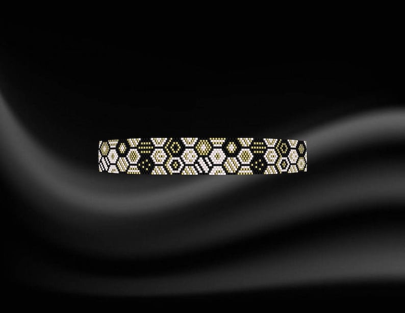 Puede incluir: Un brazalete de cuentas negras, blancas y doradas con un patr&oacute;n geom&eacute;trico.
