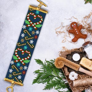 Könnte beinhalten: Ein blaues Perlenarmband mit einem Weihnachts-Zuckerstangen- und Stechpalmen-Design. Das Armband ist aus Perlen gefertigt und hat einen goldenen Verschluss.