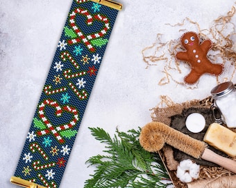 May include: A blue beaded bracelet with a Christmas candy cane and holly design. The bracelet is made with seed beads and has a gold clasp.