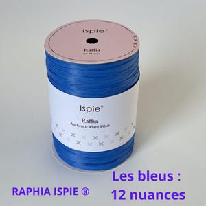 May include: A spool of blue raffia ribbon from Ispie. The label reads "Raffia Authentic Plant Fiber" and "310 Meters". The text "Les bleus: 12 nuances" is also visible. The spool is on a white surface.