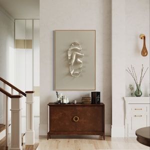 May include: A brown wooden cabinet with two doors and a gold ring pull handle. The cabinet is in a hallway with a white wall and a framed abstract art piece above it.