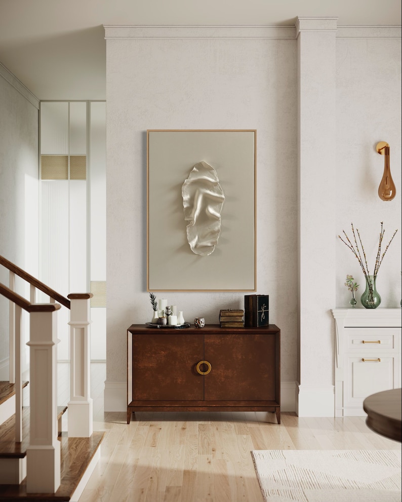 May include: A brown wooden cabinet with two doors and a gold ring pull handle. The cabinet is in a hallway with a white wall and a framed abstract art piece above it.