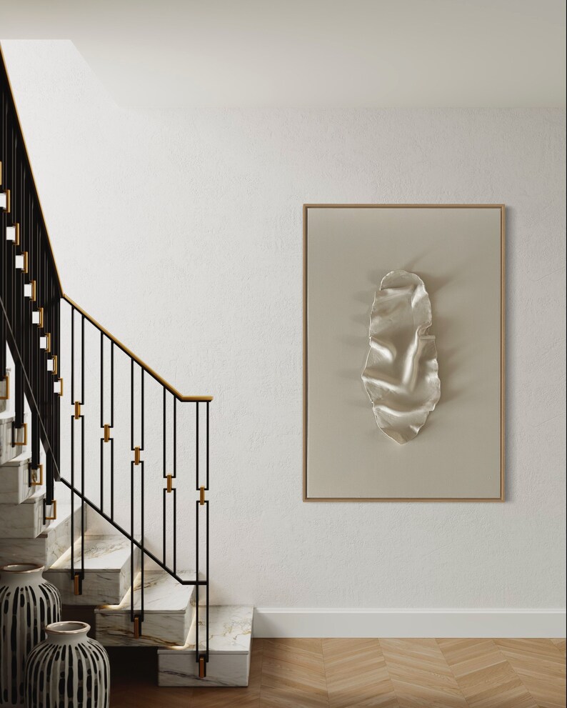 May include: A white wall with a modern staircase with black metal railings and gold accents. A framed artwork with a white textured design hangs on the wall.