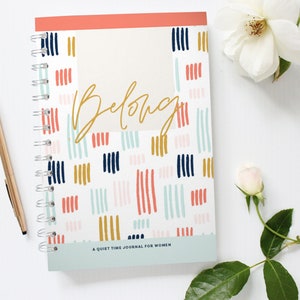 May include: A white spiral bound journal with a colorful abstract pattern and the word "Belong" in gold lettering. The text "A Quiet Time Journal for Women" is printed on the bottom of the cover.