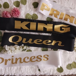 May include: Four satin sashes with gold lettering. The sashes read "King", "Queen", "Princess", and "Prince".