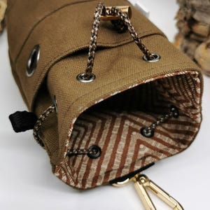 Puede incluir: Una bolsa de lona marr&oacute;n con cord&oacute;n y un interior estampado. La bolsa presenta un cord&oacute;n trenzado, ojales met&aacute;licos y un mosquet&oacute;n dorado. El forro interior tiene un dise&ntilde;o geom&eacute;trico marr&oacute;n y blanco.