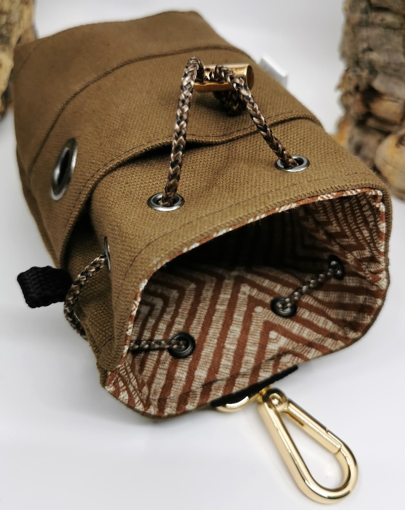 Puede incluir: Una bolsa de lona marr&oacute;n con cord&oacute;n y un interior estampado. La bolsa presenta un cord&oacute;n trenzado, ojales met&aacute;licos y un mosquet&oacute;n dorado. El forro interior tiene un dise&ntilde;o geom&eacute;trico marr&oacute;n y blanco.