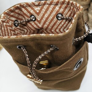 Puede incluir: Una bolsa de lona marr&oacute;n con cord&oacute;n y un interior estampado. La bolsa tiene un peque&ntilde;o bolsillo frontal y se cierra con un cord&oacute;n trenzado. El forro interior presenta un dise&ntilde;o de chevron marr&oacute;n y blanco.
