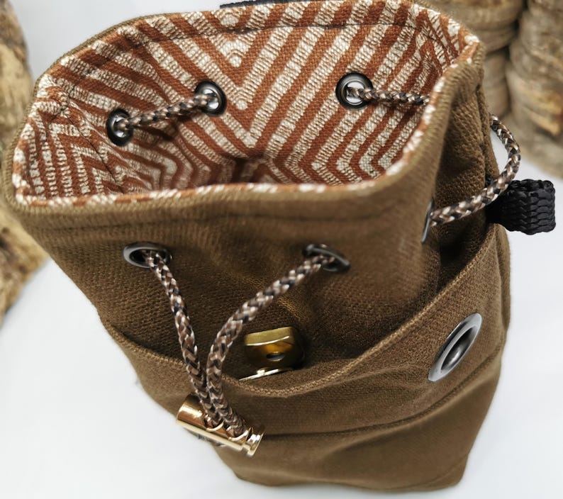 Puede incluir: Una bolsa de lona marr&oacute;n con cord&oacute;n y un interior estampado. La bolsa tiene un peque&ntilde;o bolsillo frontal y se cierra con un cord&oacute;n trenzado. El forro interior presenta un dise&ntilde;o de chevron marr&oacute;n y blanco.