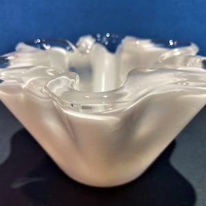 May include: A white glass bowl with a ruffled edge. The bowl is made of clear glass with a white opaque finish.