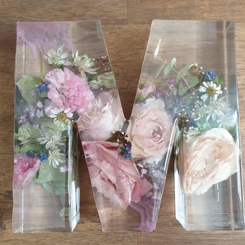 May include: A clear resin letter M filled with pressed pink and white flowers, including roses, and greenery.