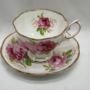 May include: A white teacup and saucer with a gold trim and pink rose floral pattern.