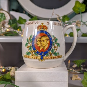 Może przedstawiać: Biały ceramiczny kubek z herbem królewskim przedstawiającym portret króla Jerzego VI i królowej Elżbiety. Herb zawiera tekst "Honi Soit Qui Mal Y Pense" i "Dieu Et Mon Droit".