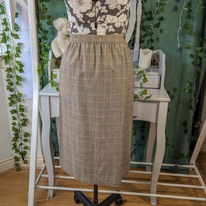 May include: A brown and white plaid skirt with a high waist and a straight silhouette. The skirt is knee-length and has a subtle sheen.
