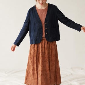 Puede incluir: Una chaqueta azul marino de manga larga con cuello en V y tres botones frontales, combinada con un top texturizado de color terracota y una falda midi a juego que presenta un sutil estampado floral en marrón oscuro en la tela.