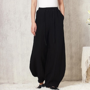 May include: Black wide-leg pants with a drawstring waist and pockets. The pants are paired with a white scoop-neck t-shirt. The outfit is casual and comfortable, suitable for everyday wear. The pants have a unique, voluminous shape.