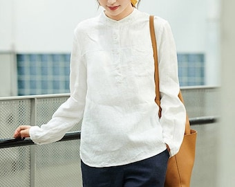 May include: A woman wearing a white linen shirt with a mandarin collar and long sleeves, paired with dark blue cropped pants and green pointed-toe heels. She is carrying a brown leather tote bag.