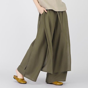 May include: A woman wearing a beige short-sleeved top and olive green wide-leg trousers. The trousers have a layered design and are made of a lightweight fabric.