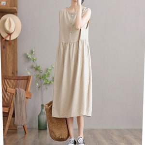 May include: A sleeveless, beige linen dress with a button-up front and a slightly gathered skirt. The dress is midi-length and has a relaxed fit.