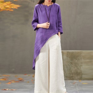 Puede incluir: Una blusa de lino morada con un dobladillo largo y asimétrico combinada con pantalones blancos de lino de pierna ancha.