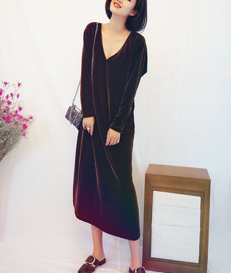 May include: A long-sleeved brown velvet dress with a V-neckline. The dress is midi-length and has a relaxed fit.