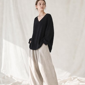 May include: A black long-sleeved shirt with a V-neckline paired with loose-fitting beige wide-leg trousers. The shirt features a relaxed fit and long sleeves, while the trousers have a straight, flowing silhouette and reach the ankles.