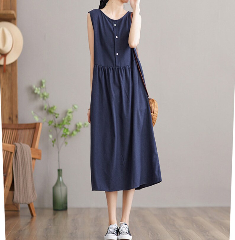 May include: A navy blue sleeveless midi dress with a button-up front and a gathered waist. The dress is made of a lightweight fabric and has a relaxed fit.