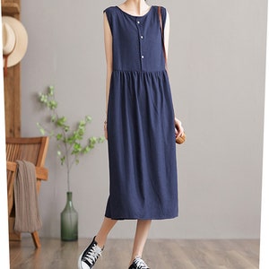 May include: A sleeveless navy blue midi dress with a single button closure at the neckline. The dress has a slightly gathered skirt and a relaxed fit.