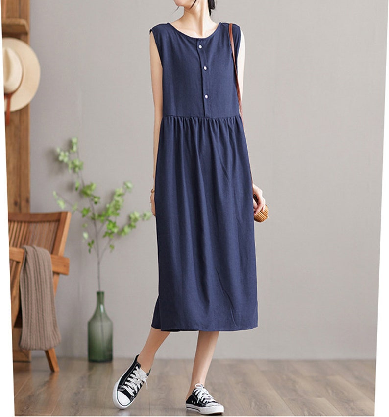 May include: A sleeveless navy blue midi dress with a single button closure at the neckline. The dress has a slightly gathered skirt and a relaxed fit.