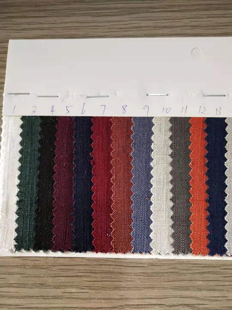 May include: A fabric swatch card with 13 different colors of linen fabric. The colors are: white, gray, orange, dark blue, light blue, brown, red, burgundy, dark blue, black, green, and white.