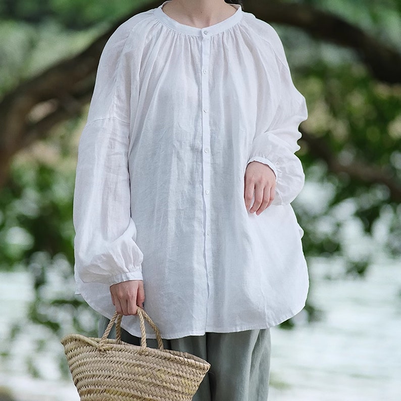May include: A white linen blouse with a round neckline and button closure. The blouse has long sleeves with gathered cuffs and a relaxed fit.