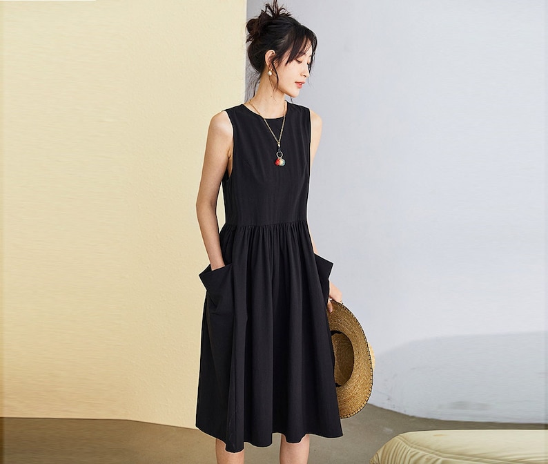 May include: A black sleeveless dress with a gathered skirt and two pockets. The dress is knee-length and has a simple, elegant design.