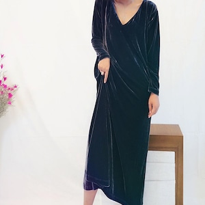 May include: A long, dark blue velvet dress with a V-neckline and long sleeves. The dress is loose-fitting and falls to the mid-calf.