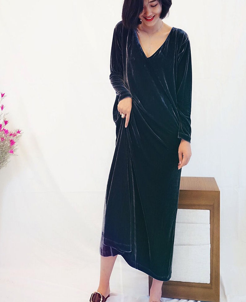 May include: A long, dark blue velvet dress with a V-neckline and long sleeves. The dress is loose-fitting and falls to the mid-calf.