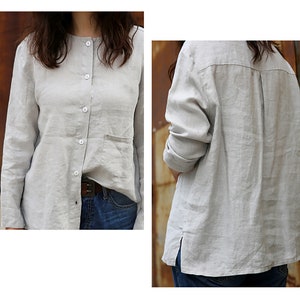 May include: A light grey linen shirt with a button-up front, long sleeves, and a single pocket on the left side. The shirt is slightly oversized and has a relaxed fit.