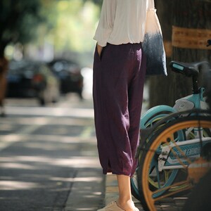 May include: A person wearing a white shirt and purple pants stands next to a teal bicycle. The bicycle has a brown tire and a white handlebar.