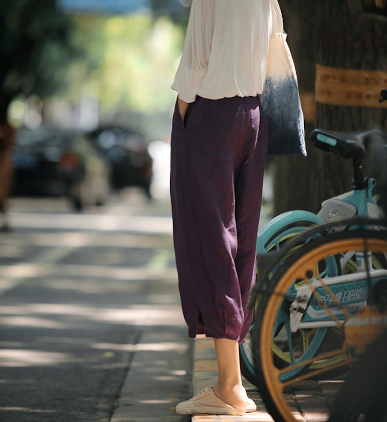 May include: A person wearing a white shirt and purple pants stands next to a teal bicycle. The bicycle has a brown tire and a white handlebar.