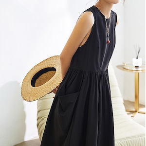 May include: A black sleeveless midi dress with a gathered waist and a large patch pocket on the left side. The dress is made of a lightweight fabric and has a relaxed fit.