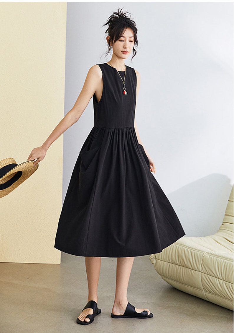 May include: A black sleeveless midi dress with a gathered waist and two pockets. The dress is made of a lightweight fabric and has a relaxed fit.