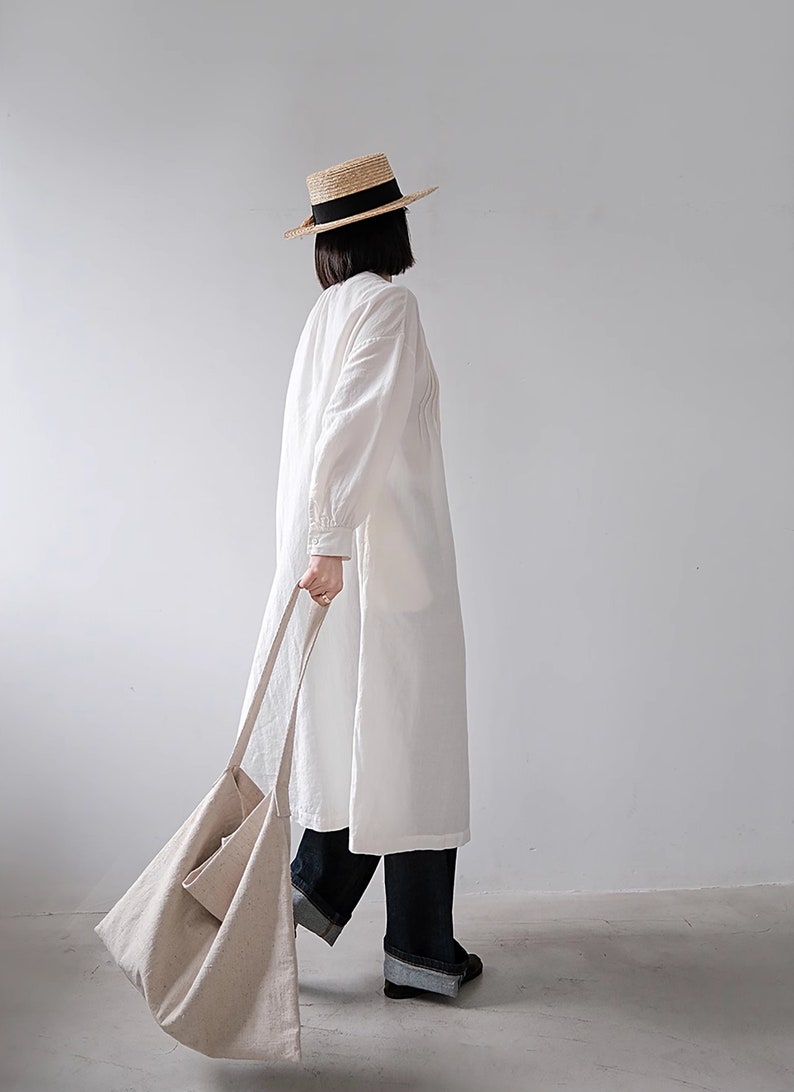 May include: A woman wearing a white linen dress with a straw hat and a beige tote bag.