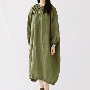 May include: A loose-fitting, long-sleeved, olive green linen dress with a keyhole neckline and gathered details at the cuffs and hem.