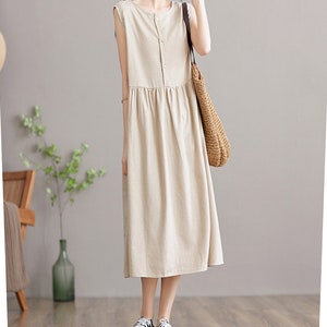 May include: A beige sleeveless linen dress with a button-up front and a gathered skirt. The dress is midi-length and has a relaxed fit.