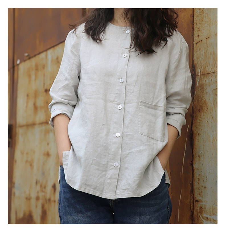 May include: A light grey linen shirt with a button-up front and a single pocket on the left chest. The shirt has long sleeves and a relaxed fit.