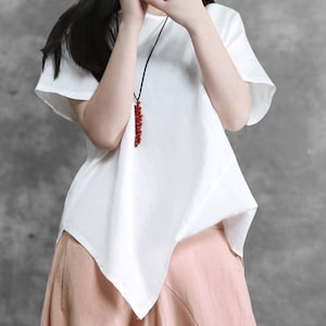 May include: White asymmetrical linen top with short sleeves and a red beaded necklace.