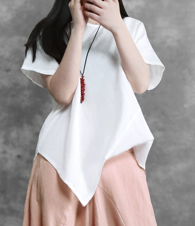 May include: White asymmetrical linen top with short sleeves and a red beaded necklace.