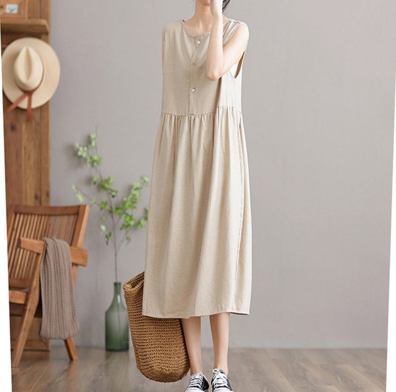 May include: A sleeveless, beige linen dress with a button-up front and a slightly gathered skirt. The dress is midi-length and has a relaxed fit.