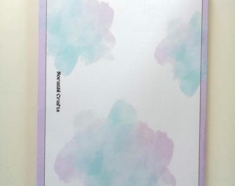 May include: A rectangular notepad with a light purple border and a white center featuring soft, watercolor-style clouds in shades of blue and purple. The text Norathi Crafts is printed vertically in black on the left side within the border.
