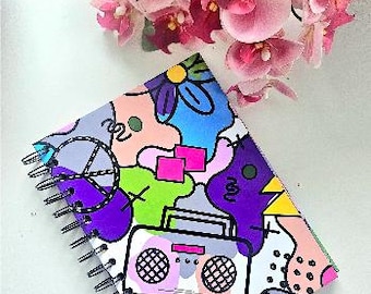 May include: A spiral-bound notebook featuring a colorful graphic print of a boombox, a peace sign, and abstract shapes in shades of blue, purple, pink, yellow, and green. The cover design includes various geometric patterns and bold black outlines.